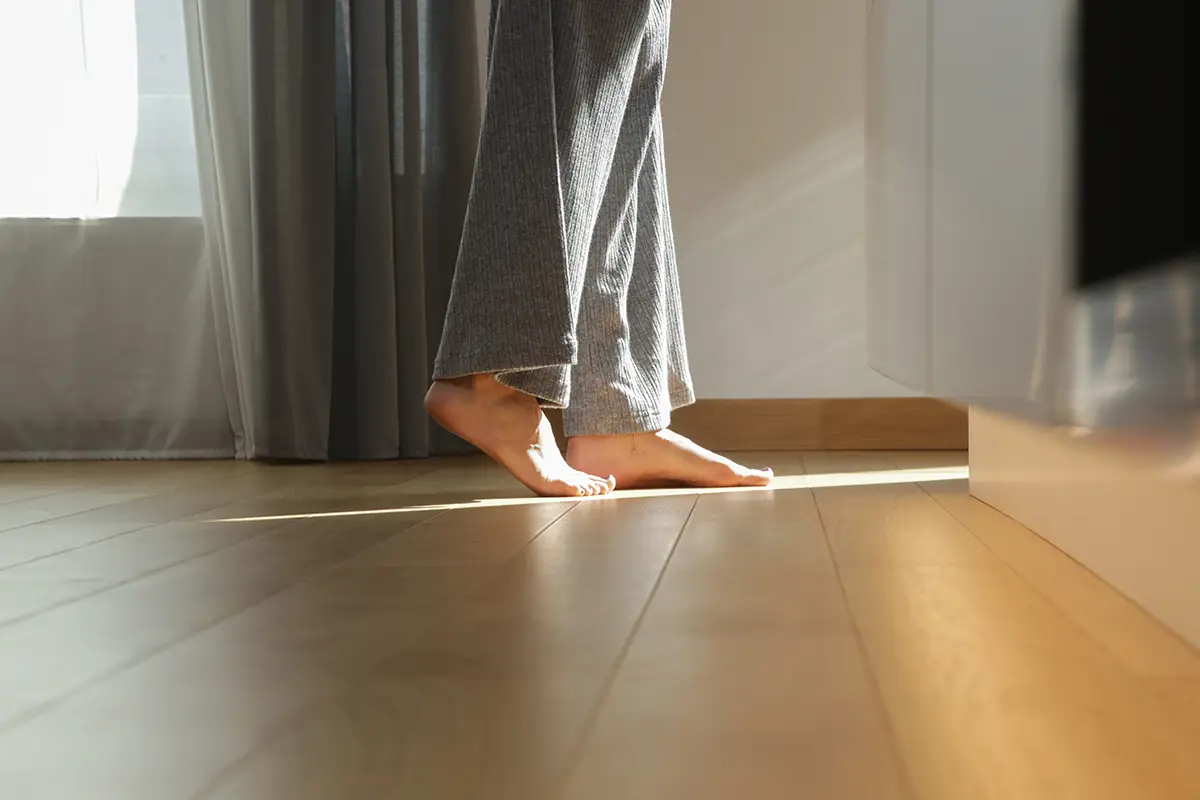 Bosé nohy na olejovanej drevenej podlahe pri jemnom osvetlení.